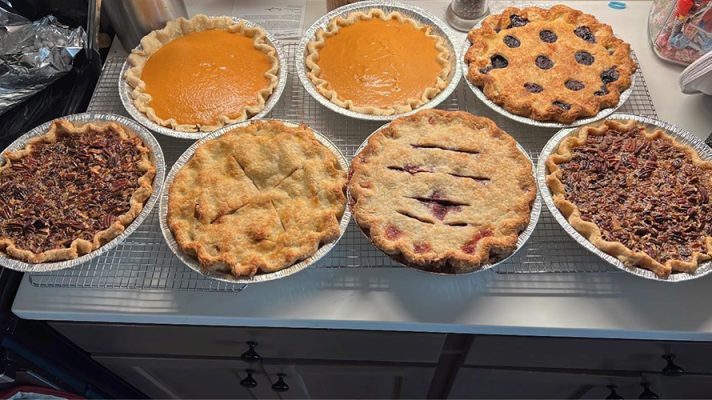 Eight homemade Blue Sky Productions pies cooling on a rack — pumpkin, blueberry, pecan, apple and cherry